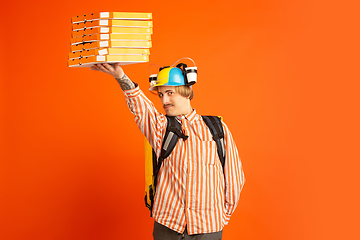 Image showing Contacless delivery service during quarantine. Man delivers food and shopping bags during insulation. Emotions of deliveryman isolated on orange background.