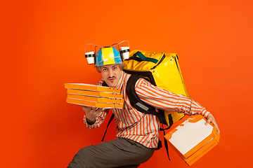 Image showing Contacless delivery service during quarantine. Man delivers food and shopping bags during insulation. Emotions of deliveryman isolated on orange background.