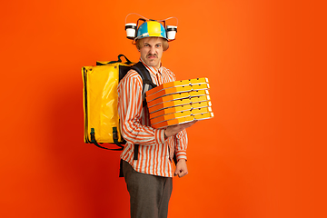 Image showing Contacless delivery service during quarantine. Man delivers food and shopping bags during insulation. Emotions of deliveryman isolated on orange background.