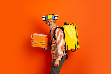 Image showing Contacless delivery service during quarantine. Man delivers food and shopping bags during insulation. Emotions of deliveryman isolated on orange background.