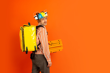 Image showing Contacless delivery service during quarantine. Man delivers food and shopping bags during insulation. Emotions of deliveryman isolated on orange background.