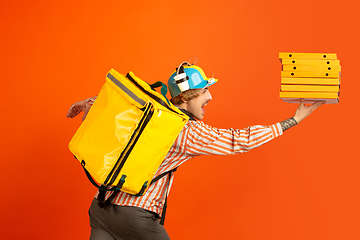 Image showing Contacless delivery service during quarantine. Man delivers food and shopping bags during insulation. Emotions of deliveryman isolated on orange background.