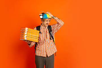 Image showing Contacless delivery service during quarantine. Man delivers food and shopping bags during insulation. Emotions of deliveryman isolated on orange background.