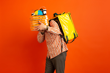 Image showing Contacless delivery service during quarantine. Man delivers food and shopping bags during insulation. Emotions of deliveryman isolated on orange background.