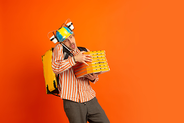 Image showing Contacless delivery service during quarantine. Man delivers food and shopping bags during insulation. Emotions of deliveryman isolated on orange background.