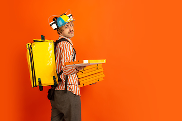 Image showing Contacless delivery service during quarantine. Man delivers food and shopping bags during insulation. Emotions of deliveryman isolated on orange background.