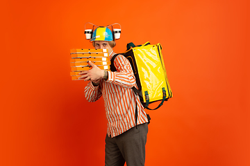 Image showing Contacless delivery service during quarantine. Man delivers food and shopping bags during insulation. Emotions of deliveryman isolated on orange background.