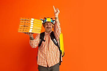 Image showing Contacless delivery service during quarantine. Man delivers food and shopping bags during insulation. Emotions of deliveryman isolated on orange background.