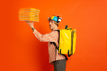 Image showing Contacless delivery service during quarantine. Man delivers food and shopping bags during insulation. Emotions of deliveryman isolated on orange background.