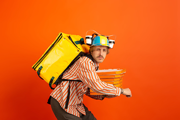 Image showing Contacless delivery service during quarantine. Man delivers food and shopping bags during insulation. Emotions of deliveryman isolated on orange background.