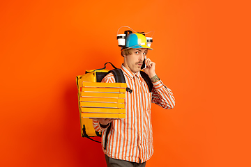 Image showing Contacless delivery service during quarantine. Man delivers food and shopping bags during insulation. Emotions of deliveryman isolated on orange background.