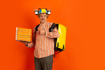 Image showing Contacless delivery service during quarantine. Man delivers food and shopping bags during insulation. Emotions of deliveryman isolated on orange background.