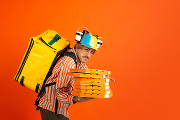 Image showing Contacless delivery service during quarantine. Man delivers food and shopping bags during insulation. Emotions of deliveryman isolated on orange background.