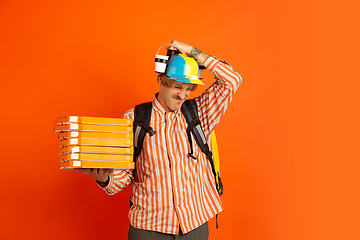 Image showing Contacless delivery service during quarantine. Man delivers food and shopping bags during insulation. Emotions of deliveryman isolated on orange background.