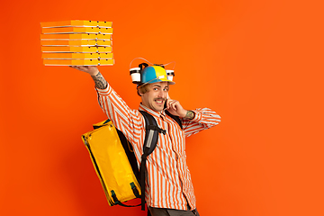 Image showing Contacless delivery service during quarantine. Man delivers food and shopping bags during insulation. Emotions of deliveryman isolated on orange background.