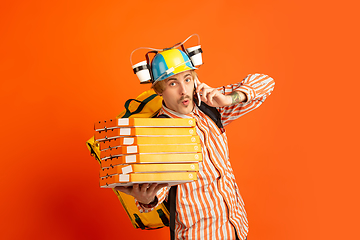 Image showing Contacless delivery service during quarantine. Man delivers food and shopping bags during insulation. Emotions of deliveryman isolated on orange background.