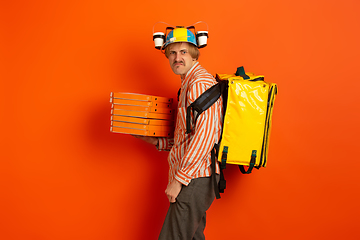 Image showing Contacless delivery service during quarantine. Man delivers food and shopping bags during insulation. Emotions of deliveryman isolated on orange background.