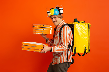 Image showing Contacless delivery service during quarantine. Man delivers food and shopping bags during insulation. Emotions of deliveryman isolated on orange background.