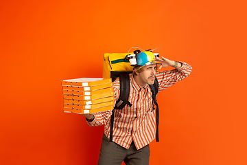 Image showing Contacless delivery service during quarantine. Man delivers food and shopping bags during insulation. Emotions of deliveryman isolated on orange background.