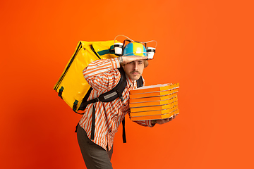 Image showing Contacless delivery service during quarantine. Man delivers food and shopping bags during insulation. Emotions of deliveryman isolated on orange background.