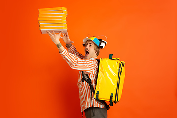 Image showing Contacless delivery service during quarantine. Man delivers food and shopping bags during insulation. Emotions of deliveryman isolated on orange background.