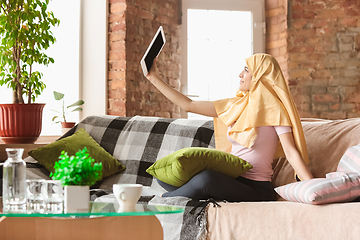 Image showing A pretty young muslim woman at home during quarantine and self-insulation, using tablet for selfie or videocall, online lessons