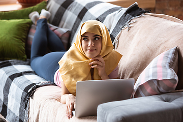 Image showing A pretty young muslim woman at home during quarantine and self-insulation, using laptop, listen to music, watching cinema, serials, shopping, studying