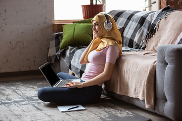 Image showing A pretty young muslim woman at home during quarantine and self-insulation, using laptop, listen to music, watching cinema, serials, shopping, studying