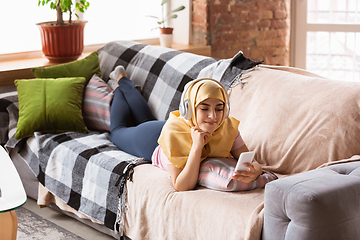 Image showing A pretty young muslim woman at home during quarantine and self-insulation, using headphones, listen to music, watching cinema, serials, enjoying