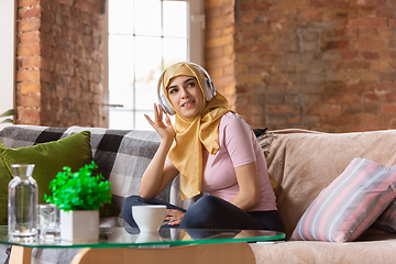 Image showing A pretty young muslim woman at home during quarantine and self-insulation, using headphones, listen to music, enjoying