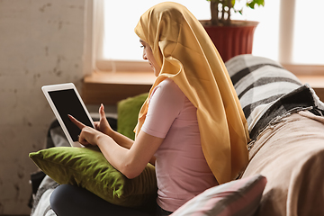 Image showing A pretty young muslim woman at home during quarantine and self-insulation, using tablet for selfie or videocall, online lessons