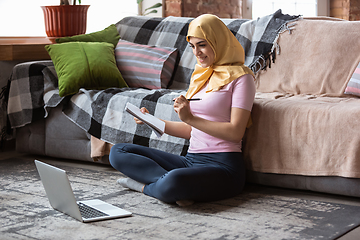 Image showing A pretty young muslim woman at home during quarantine and self-insulation, using laptop, listen to music, watching cinema, serials, shopping, studying