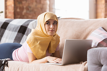 Image showing A pretty young muslim woman at home during quarantine and self-insulation, using laptop, listen to music, watching cinema, serials, shopping, studying