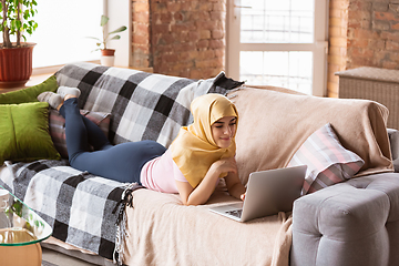 Image showing A pretty young muslim woman at home during quarantine and self-insulation, using laptop, listen to music, watching cinema, serials, shopping, studying