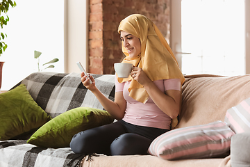 Image showing A pretty young muslim woman at home during quarantine and self-insulation, using smartphone for selfie or videocall, online lessons, shopping