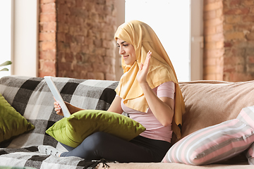 Image showing A pretty young muslim woman at home during quarantine and self-insulation, using tablet for selfie or videocall, online lessons