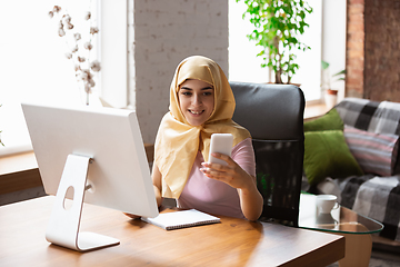 Image showing A pretty young muslim woman at home during quarantine and self-insulation, remote working, shopping, studying, watching cinema