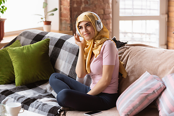 Image showing A pretty young muslim woman at home during quarantine and self-insulation, using headphones, listen to music, enjoying