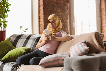 Image showing A pretty young muslim woman at home during quarantine and self-insulation, using smartphone for selfie or videocall, online lessons, shopping