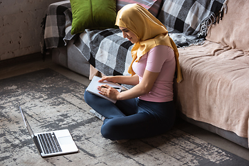 Image showing A pretty young muslim woman at home during quarantine and self-insulation, using laptop, listen to music, watching cinema, serials, shopping, studying