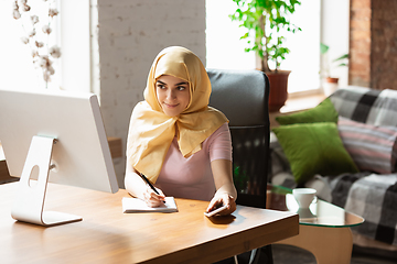 Image showing A pretty young muslim woman at home during quarantine and self-insulation, remote working, shopping, studying, watching cinema