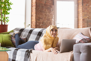 Image showing A pretty young muslim woman at home during quarantine and self-insulation, using laptop, listen to music, watching cinema, serials, shopping, studying