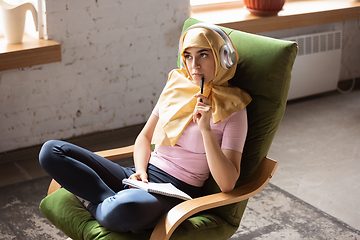 Image showing A pretty young muslim woman at home during quarantine and self-insulation, using headphones, listen to music, enjoying