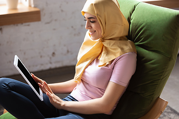 Image showing A pretty young muslim woman at home during quarantine and self-insulation, using tablet for selfie or videocall, online lessons, shopping