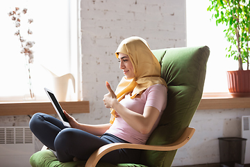 Image showing A pretty young muslim woman at home during quarantine and self-insulation, using laptop for videocall, watching cinema, serials, shopping, studying