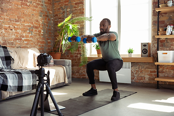 Image showing Young african-american man teaching at home online courses of fitness, aerobic, sporty lifestyle during quarantine, reording on camera, streaming