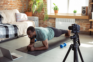 Image showing Young african-american man teaching at home online courses of fitness, aerobic, sporty lifestyle during quarantine, reording on camera, streaming