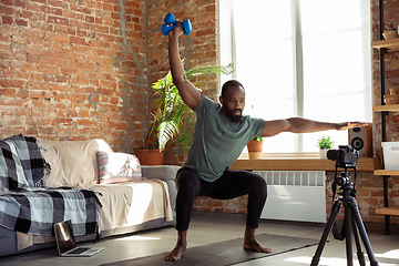 Image showing Young african-american man teaching at home online courses of fitness, aerobic, sporty lifestyle during quarantine, reording on camera, streaming