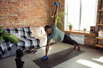 Image showing Young african-american man teaching at home online courses of fitness, aerobic, sporty lifestyle during quarantine, reording on camera, streaming