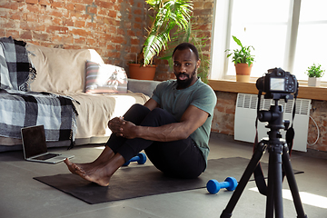 Image showing Young african-american man teaching at home online courses of fitness, aerobic, sporty lifestyle during quarantine, reording on camera, streaming